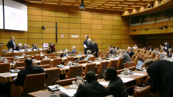 The picture shows the meeting room, which has light brown wooden paneled walls and brown leather chairs. In the picture are meeting attendees in discussion.