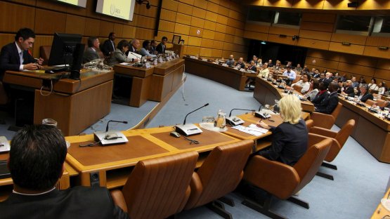 The picture shows the meeting room, which has light brown wooden paneled walls and brown leather chairs. In the picture the meeting is in session.